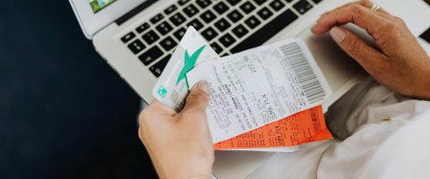Close-up of hands holding receipts and a bank card in front of a laptop, representing online shopping and e-commerce.