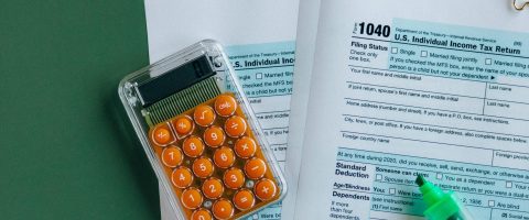 1040 tax forms with calculator, pencils, and markers on green surface.