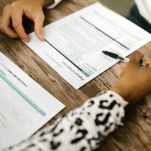 Close-up of two people reviewing and filling out a credit card application on a wooden table.